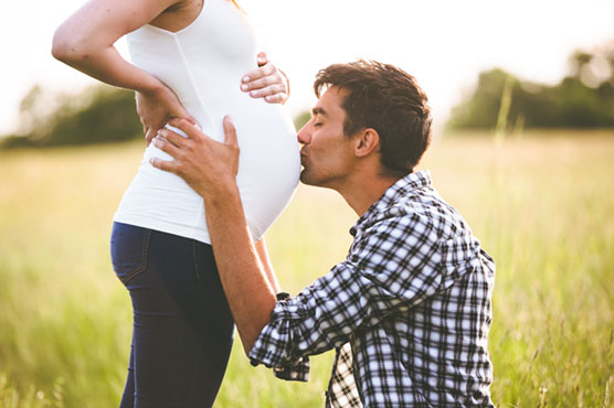 Mann küsst den Babybauch einer Frau